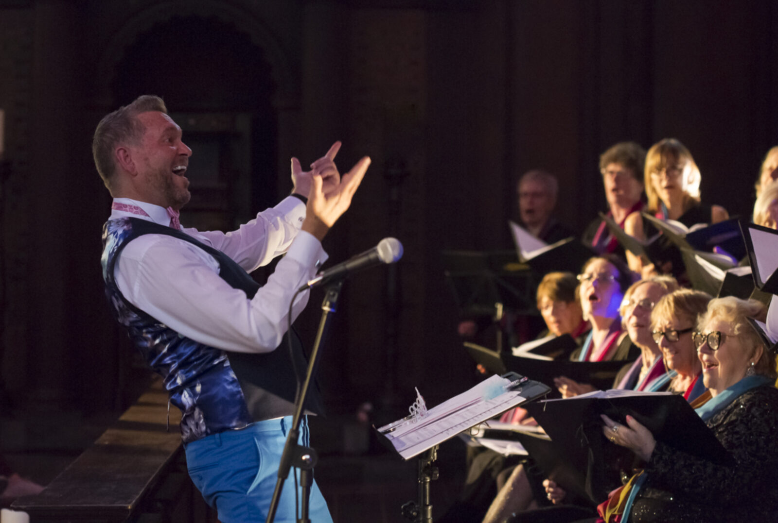 Cliff conducting a choir mid-performance, with members visible singing in the background